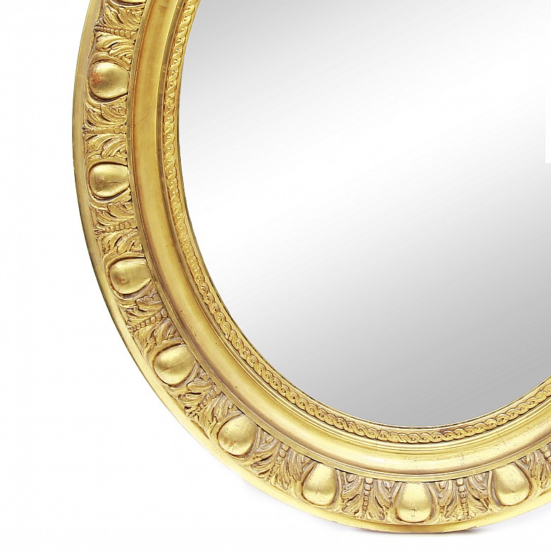 Espejo oval con marco de madera dorada.